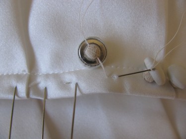a close up of stitching a satin covered button on a wedding dress